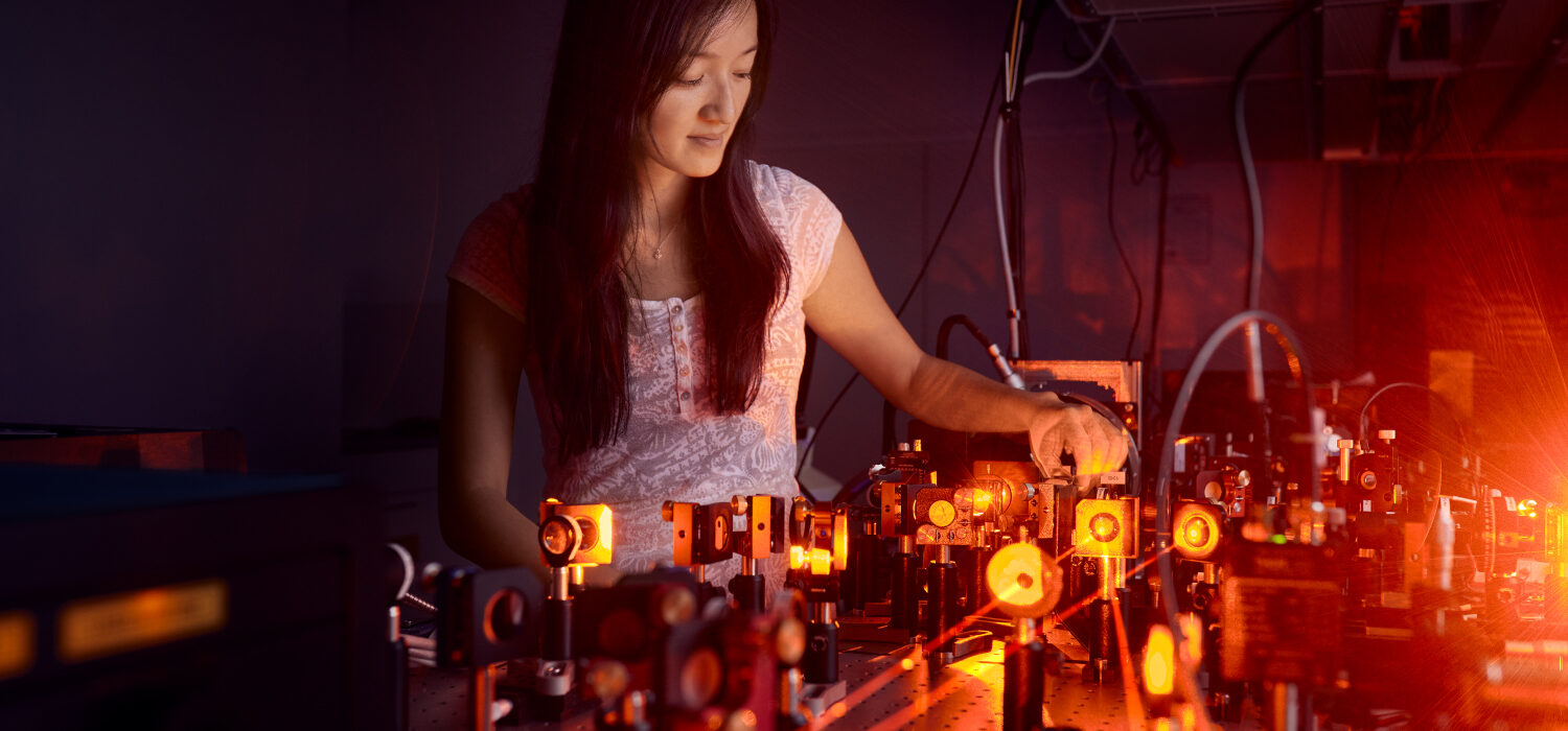 A woman in front of an experiment with lenses and lasers.