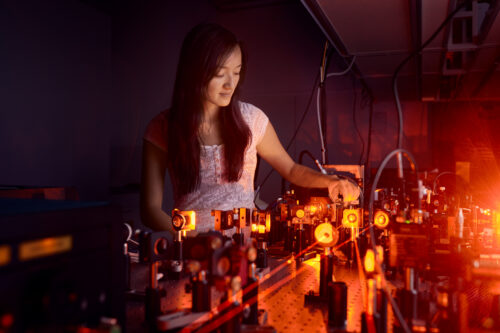 Eine Frau steht an einem Experiment mit Lasern, die durch Linsen geleitet werden.